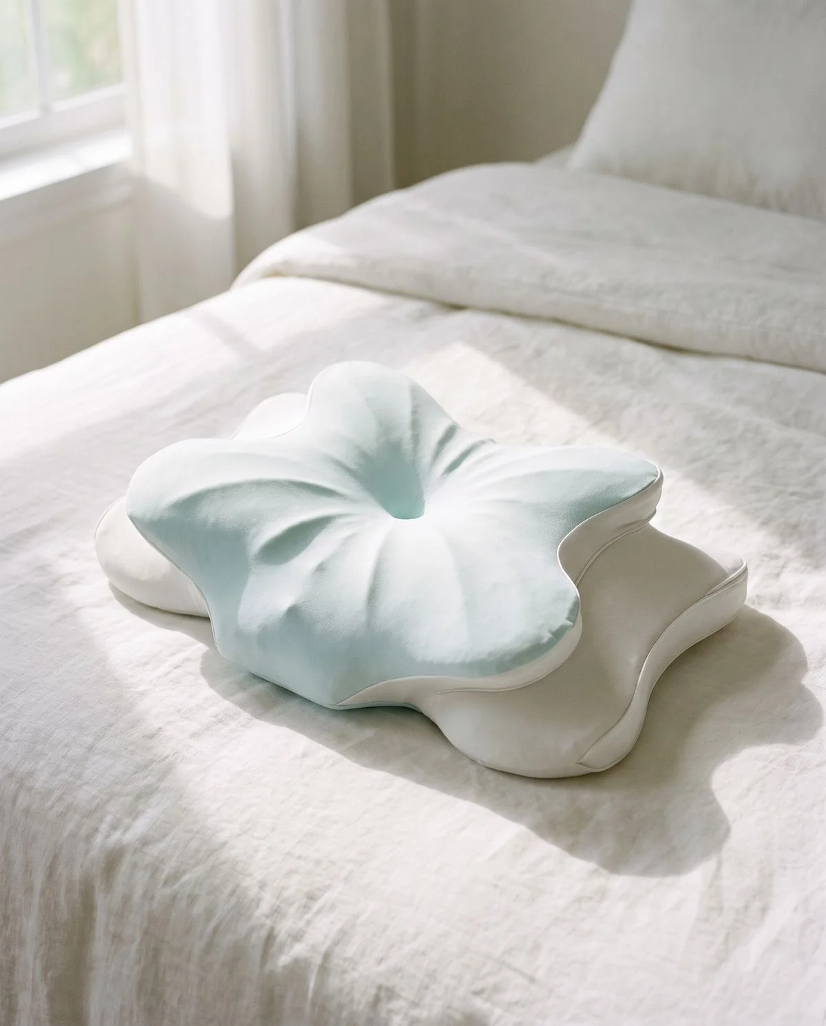 A contoured butterfly-shaped pillow with deep shoulder cut-outs, resting on a made bed in a sunlit bedroom.